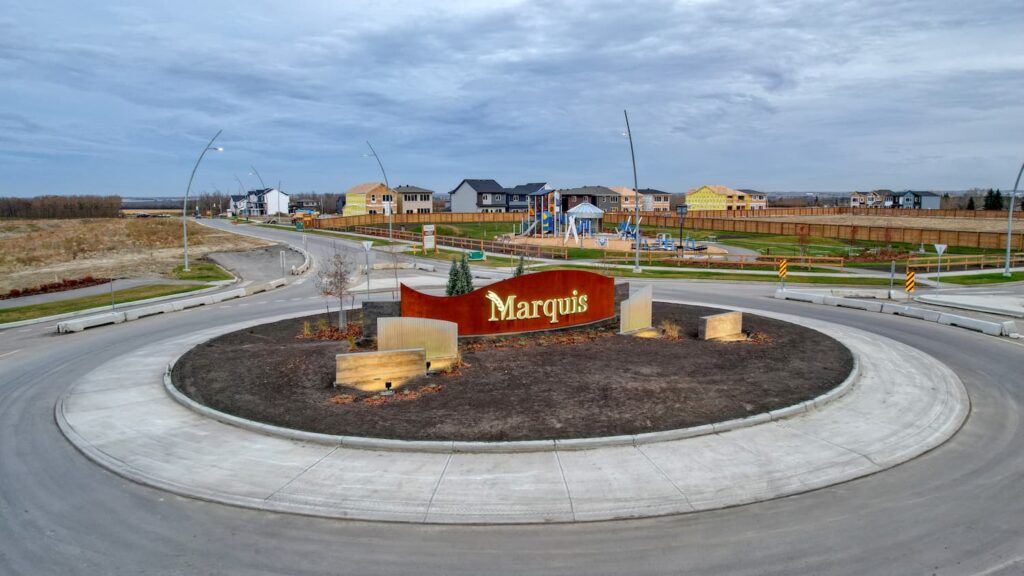 Marquis neighborhood entrance sign on traffic circle roundabout with new homes under construction and playground visible in background