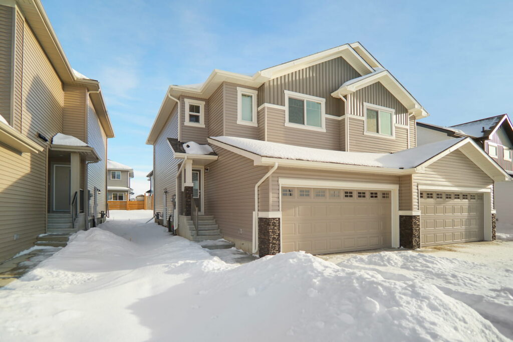 Contemporary duplex homes in Edmonton with vinyl siding, attached garages, and modern architecture in a winter setting, showcasing an affordable first-time homebuyer option