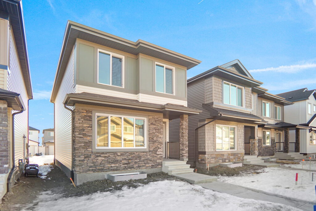 Two-story laned homes under construction in Edmonton, featuring stone and vinyl siding exteriors with rear lane access, showcasing the affordable new home style's compact design